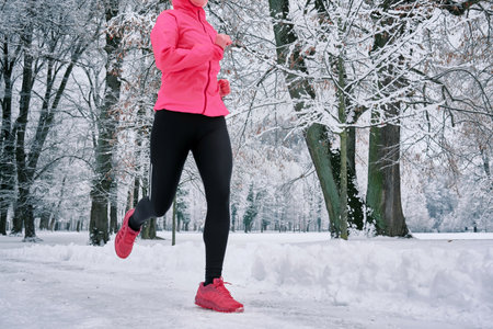 Running woman, girl runner on snow in park in winter sunny day. Female in pink sportswear jacket fitness training outdoors. Run, Sport concept, leisure and freedom.の写真素材