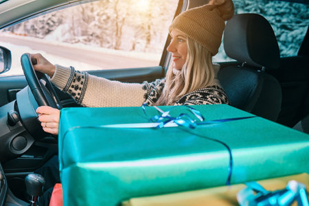Woman Giving Gifts. Female is holding presents and delivering them on her car to Home. Holidays concept. Driving car in Christmas Eve. People In A Snow-Covered Forest. Sunny Cold Winter Day.の写真素材