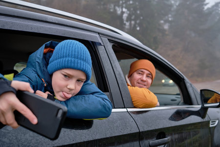 Happy father and son Sitting together in a new car on a journey. Family are resting on the side of the road on a road trip. Child takes pictures on smartphone. Happy family travels.の写真素材