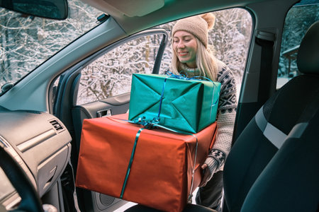Woman Giving Gifts. Female is holding presents and delivering them on her car to Home. Holidays concept. Driving car in Christmas Eve. People In A Snow-Covered Forest. Sunny Cold Winter Day.の写真素材