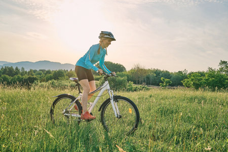Cyclist Woman riding bike in helmets go in sports outdoors on sunny day a mountain in the forest. Silhouette female at sunset. Fresh air. Health care, authenticity, sense of balance and calmness.の写真素材