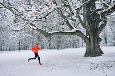 Running woman, girl runner on snow in park in winter sunny day. Female in pink sportswear jacket fitness training outdoors. Run, Sport concept, leisure and freedom.の写真素材