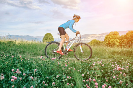 Cyclist Woman riding bike in helmets go in sports outdoors on sunny day a mountain in the forest. Silhouette female at sunset. Fresh air. Health care, authenticity, sense of balance and calmness.の写真素材