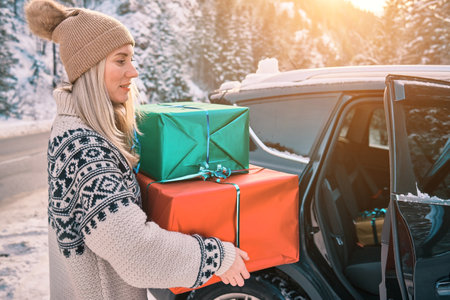 Woman Giving Gifts. Female is holding presents and delivering them on her car to Home. Holidays concept. Driving car in Christmas Eve. People In A Snow-Covered Forest. Sunny Cold Winter Day.の写真素材