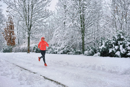 Running woman, girl runner on snow in park in winter sunny day. Female in pink sportswear jacket fitness training outdoors. Run, Sport concept, leisure and freedom.の写真素材