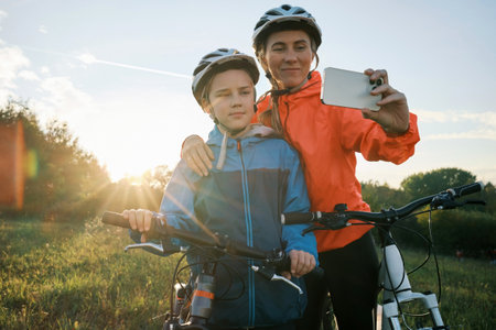 Mother and son ride a bike. Happy cute boy in helmet learn to riding a bike in park on green meadow in autumn day at sunset time. Family weekend. 4K video, Slow motionの写真素材