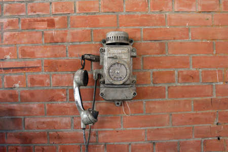 Old metal telephone on a brick wall. The text on the phone in Russian - "When calling the dispatcher, press the lever down."の写真素材