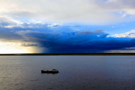 Fishing boat on the Khatanga river against the backdrop of a thundercloud. Krasnoyarsk region. Russiaの写真素材