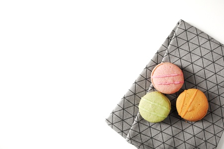 Three france cakes on a gray kitchen towel. Towel with ornament lines, boxes. Macaroons on table. Green, pink and orange sweets in circle. Close-up tasty french pastries.の写真素材