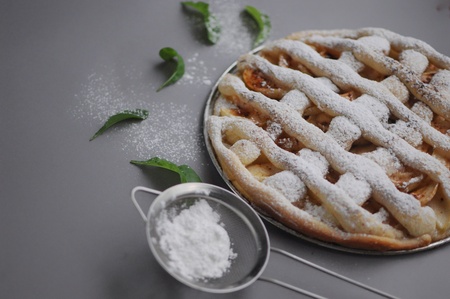 Apple pie with white towel on gray background. Dessert. Homemade cake with sieve. Autumn flatlay. Autumn homemade piece of cake with mint and sugar powder.の写真素材