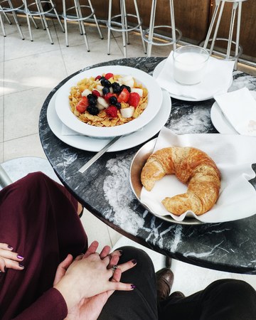 Couple man and woman is having breakfast in cafe. Couple holding hands. Beautiful breakfast: muesli,...