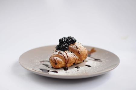 Croissant with blackberry, chocolate and powdered sugar on grey plate on white background