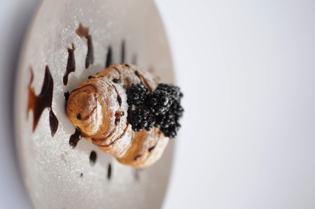 Croissant with blackberry, chocolate and powdered sugar on grey plate on white background