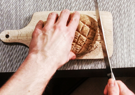 Male cuts homemade bread on wooden standの写真素材