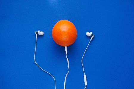 Art flat lay on classic blue background. Orange with headphones. Loading fresh music.の写真素材