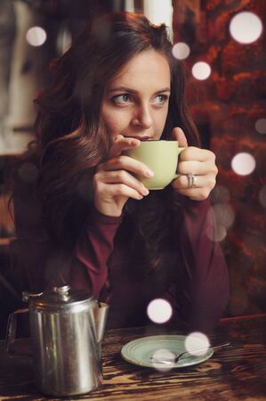 Beautiful woman sitting in the cafe, drink coffee and looking at the window.