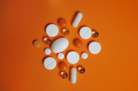 Scattered a lot of colorful pills on orange table. Medicine against COVID-19