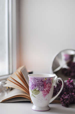 Romantic home atmosphere with a cup of tea on with lilac bush and a book.