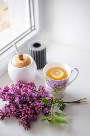 Cozy morning with cup of lemon tea composition. Lilac flowers on the windowsill