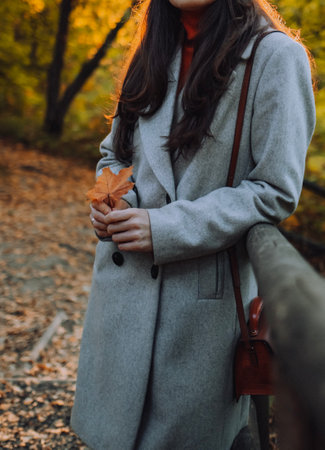 Close up of womans coat at the street without face. Girl with maple leaf in fall