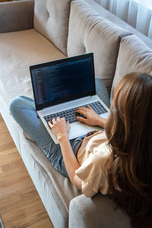 Woman working on a laptop while sitting on the sofa. A girl programmer is coding
