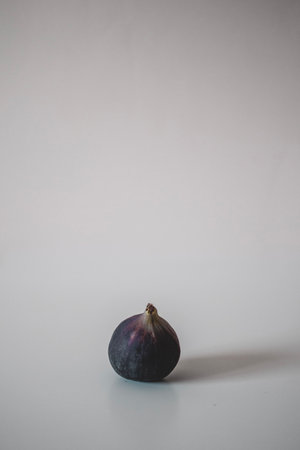 One fresh ripe fig on the table on gray background. Minimalism decor.