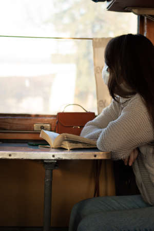 A young woman in medical mask is traveling by train alone. Taking precautions