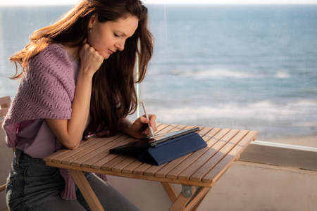 A woman artist is drawing on digital tablet on the terrace near the seaの写真素材