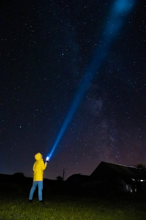 A young woman in a yellow raincoat is lighting up into the starry sky at night with torch