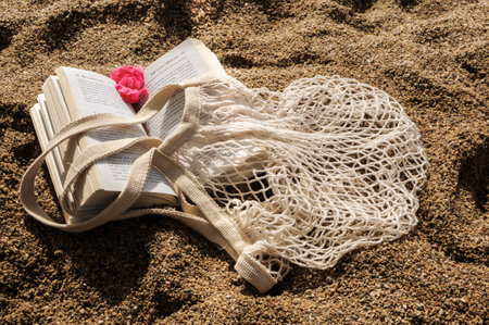 Summer flat lay on a sandy beach. Eco-friendly mesh shopping bag and a book.