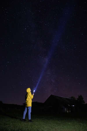 Young woman in yellow raincoat is lighting up into the starry sky with torchの写真素材