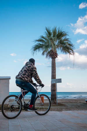 African man is riding a bike near the sea and palm tree in Larnaca, Cyprusの写真素材