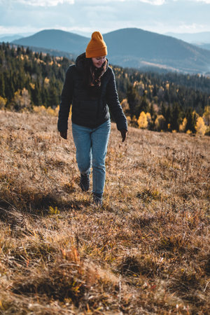 Young happy woman in orange beanie is walking in front of mountains landscapeの写真素材