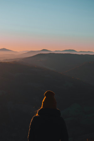 Woman from behind standing and looking away at the mountain landscape in morningの写真素材