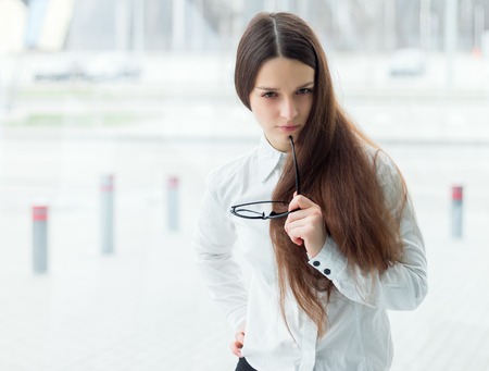 Young business woman standing in office hold glasses. Young female manager portrait.の写真素材