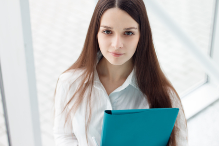 Young female manager portrait. Business woman standing in office and holding folderの写真素材