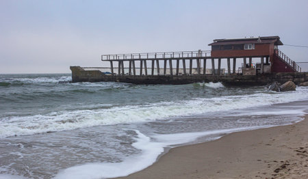 Shore and waves in the foreground and a pier of boards and concrete in the backgroundの写真素材
