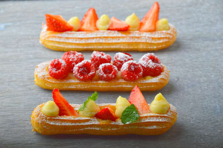 Tasty eclairs with strawberries and mint on grey table, closeup