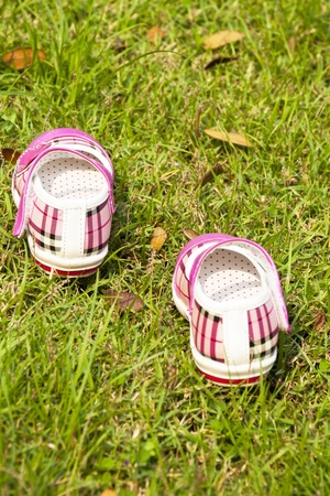 little girl shoes that are pink sitting together on a brick wall next to grassの写真素材