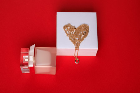 A gift for Valentine's Day. Perfume and a box with a gold chain on a red background.の写真素材