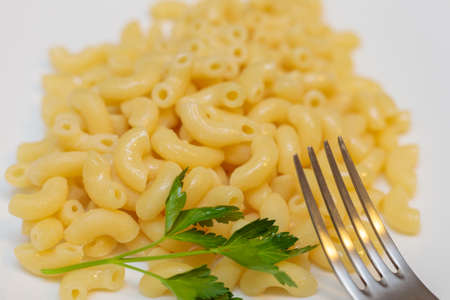 Boiled yellow pasta on a white plate with a fork. Close-up.