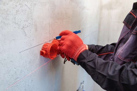 A man, an electrician marks out holes for sockets with a pencil, a tape measureの写真素材