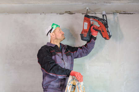 An electrician nails a wire holder to the ceiling. Repair of apartments.
