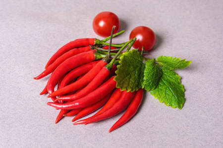 Slide of red chili peppers with one red tomato on a light background.の写真素材