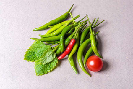 Slide of green chili peppers with one red tomato on a light background.の写真素材