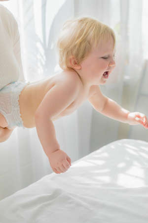 Mom does childrens gymnastics for the baby, holding him by the chest. Close-up