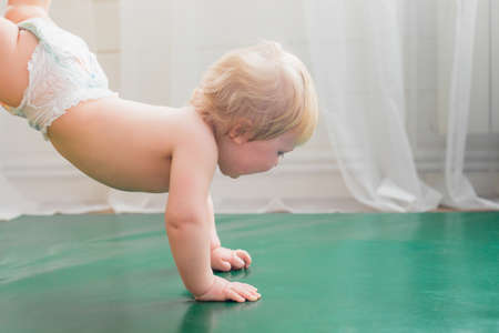 Mom holds the baby by the legs, the baby walks on the rug in her arms.