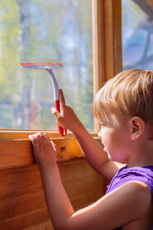 The child washes the windows with a special brush. A child with blond hairの写真素材