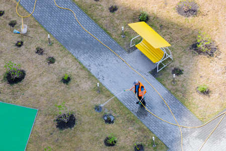 A worker is watering the bushes in the yard with a hose from the hot sun.の写真素材