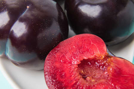 On a white saucer is a large plum, cut in half, and next to it is a whole plum.